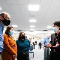 Scholar giving poster presentation to three guests, all wearing masks.